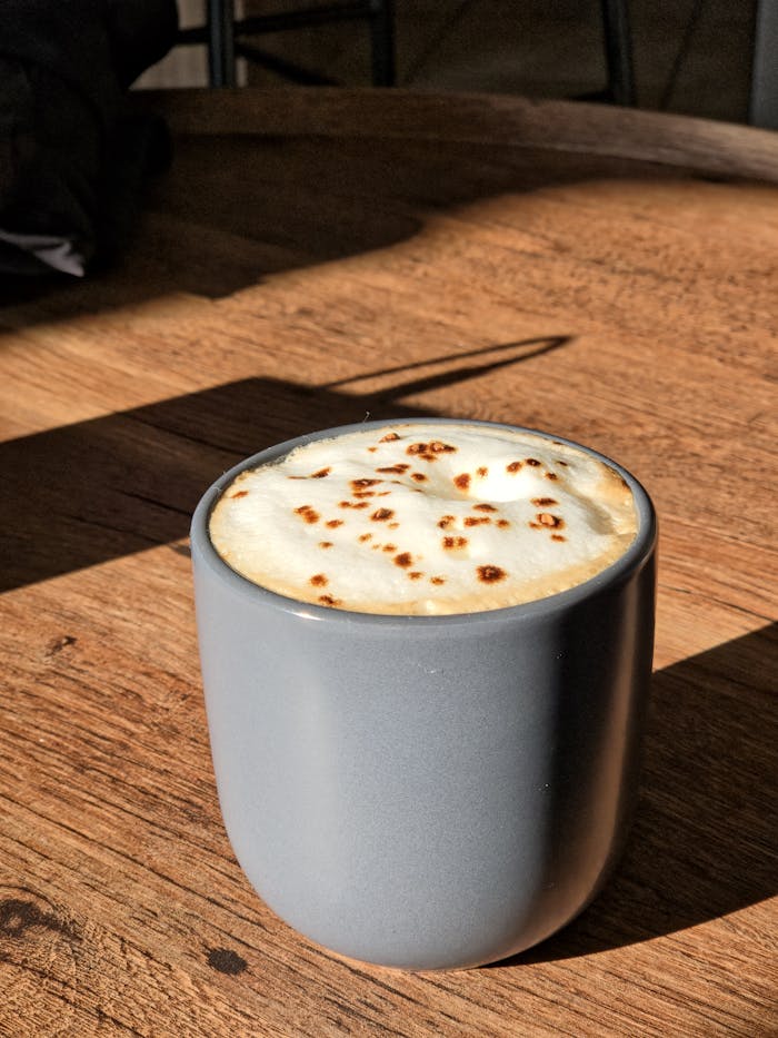 A warm cappuccino in a stylish cup with sunlight casting shadows, perfect for a cozy moment.