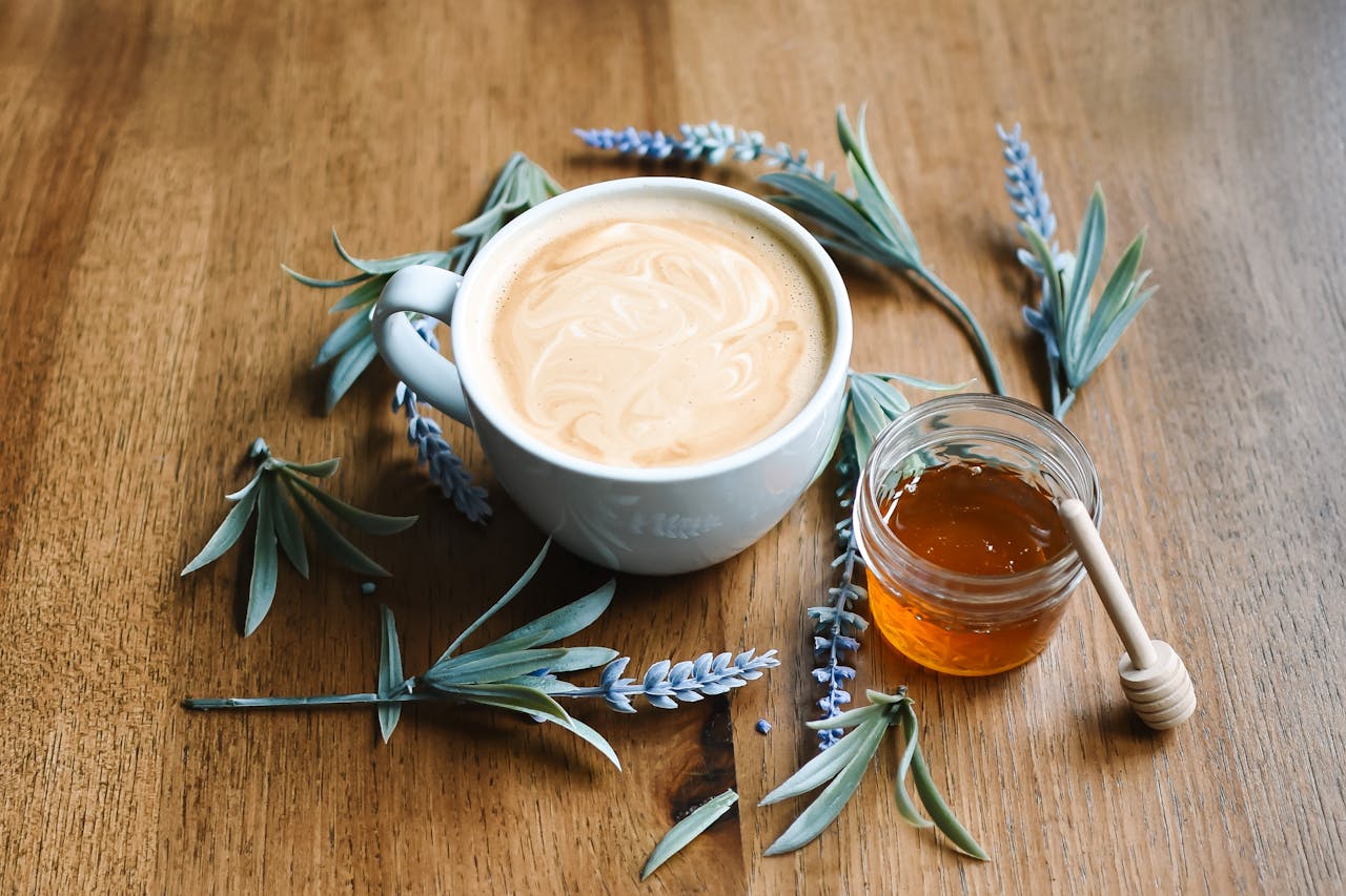 Aesthetic flat lay of a coffee cup, honey jar, and lavender sprigs on a wooden table.